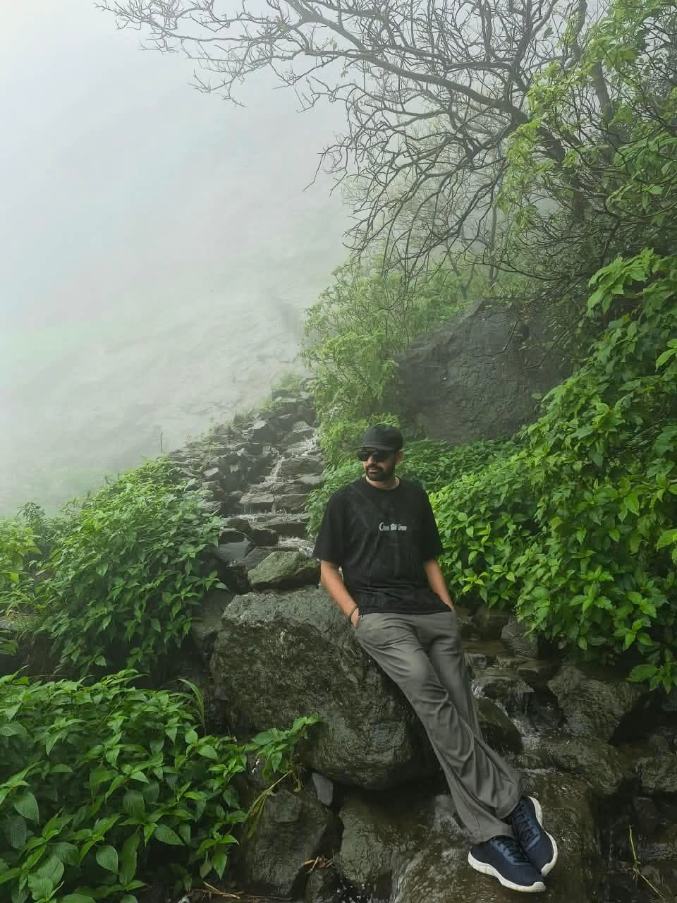 A trekker resting on a rock beside the stone steps of the misty Naneghat trail